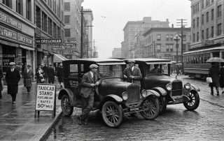 1920s Portland taxicabs beside streetcar on rainy downtown street - The History of Taxi Drivers in Portland